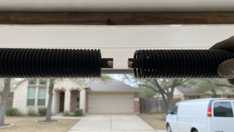 Clean break and finger-width gap in a torsion spring coil on the shaft above a double garage door