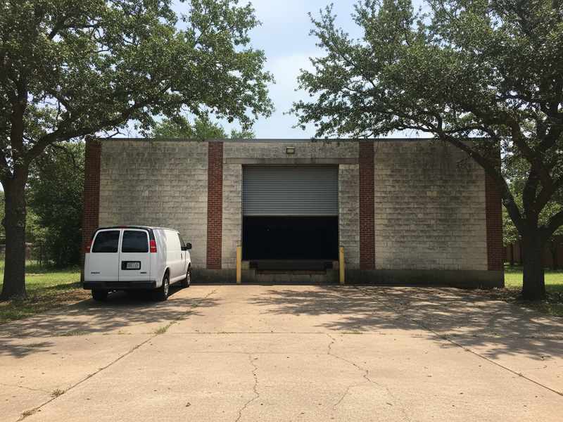 Rolling steel service door half raised at a small concrete block warehouse unit in Round Rock TX