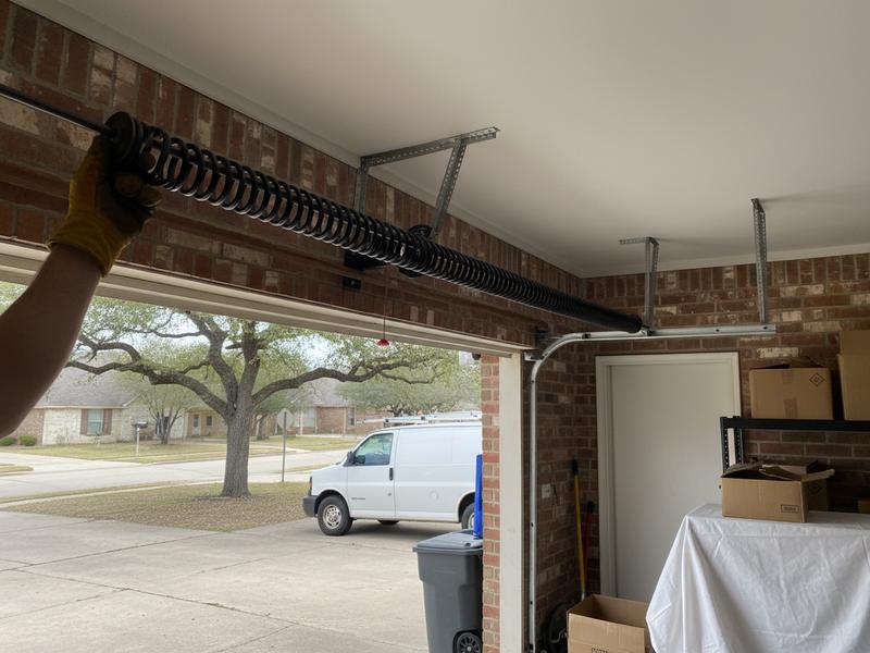 Torsion spring on the shaft above an open garage door with a winding bar set in the cone